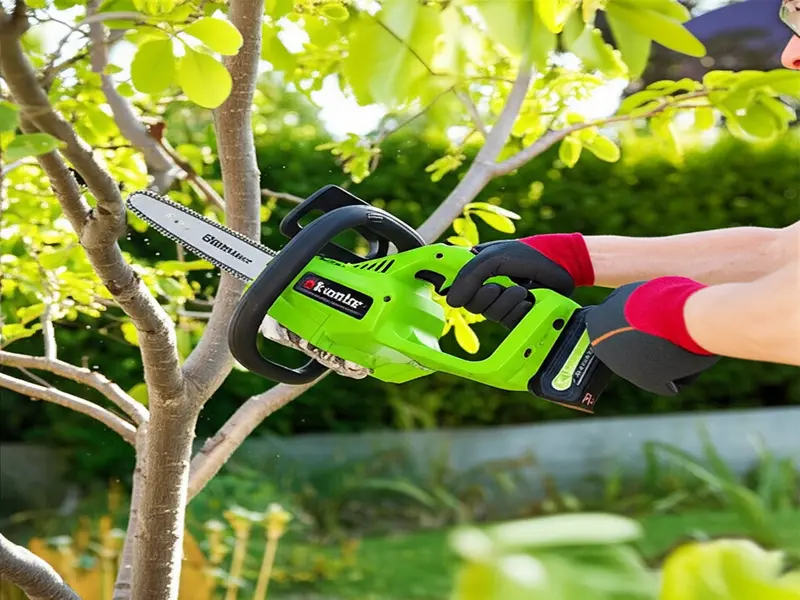 A person operating a lightweight cordless chainsaw to trim branches in a garden.